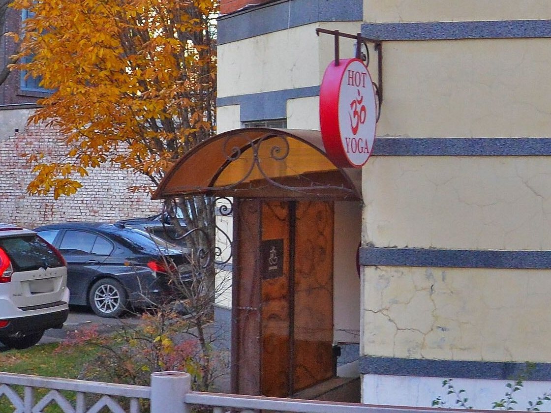 Вход в цокольный этаж: деревянная дверь под кованым козырьком, над ней круглая красная вывеска